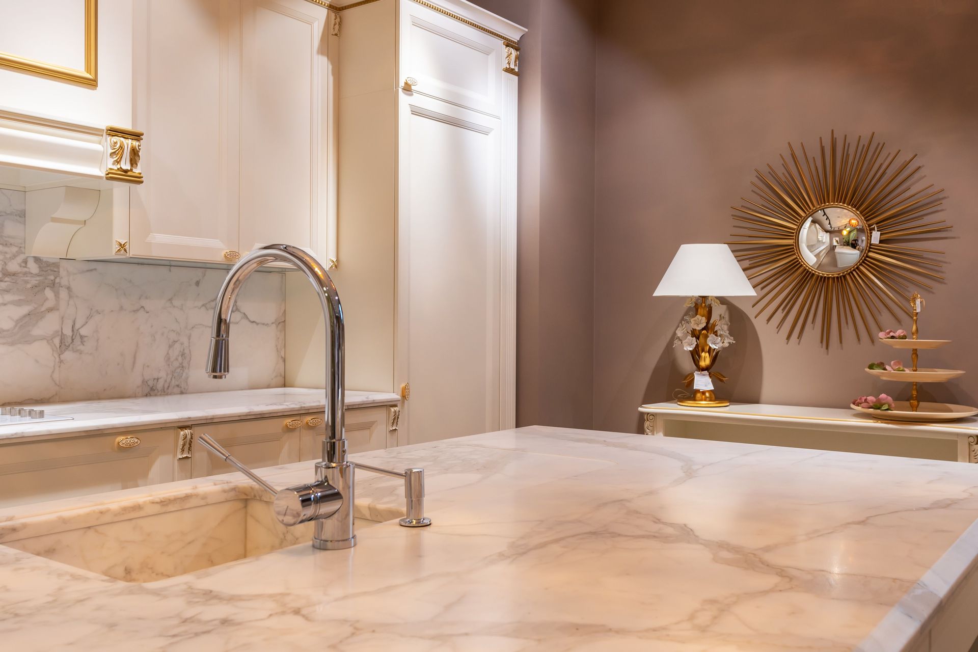 Sink with faucet on marble counter in modern stylish kitchen with white cabinets and glowing lamp near decorations in apartment